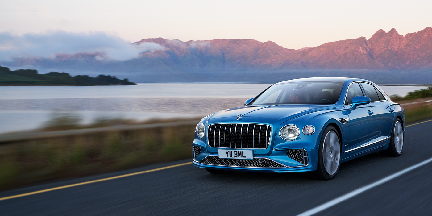Bach Premium Cars GmbH | Bentley Mannheim New Bentley Flying Spur Azure sedan in Light windsor blue paint by Mulliner, with 22 inch Azure wheels and chrome straight vaned grille driving on a mountain road