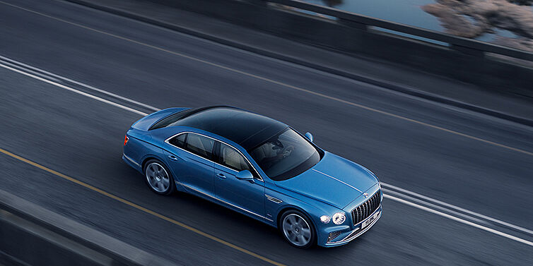 Bach Premium Cars GmbH | Bentley Mannheim New Bentley Flying Spur Azure sedan in Light windsor blue paint by Mulliner, with 22 inch Azure wheels seen from overhead driving dynamically on a country road