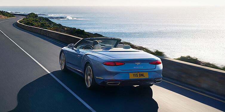 Bach Premium Cars GmbH | Bentley Mannheim New Bentley Continental GTC Azure convertible rear view in Light Windsor blue paint with 22 inch ten spoke wheels driving dynamically on an ocean road in the sunshine