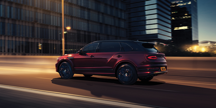 Bach Premium Cars GmbH | Bentley Mannheim Bentley Bentayga Extended Wheelbase Mulliner SUV in Cricket Ball red paint driving dynamically in city at night